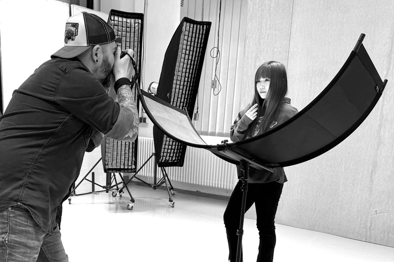 Workshop-Teilnehmerin steht Modell im Studio, während der Trainer, ein professioneller Fotograf, sie fotografiert und Anweisungen gibt.